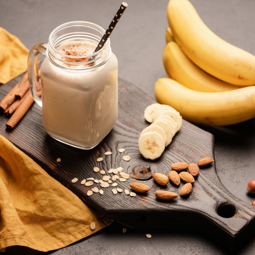 Banana protein smoothie on a wooden board with bananas, almonds, and oats